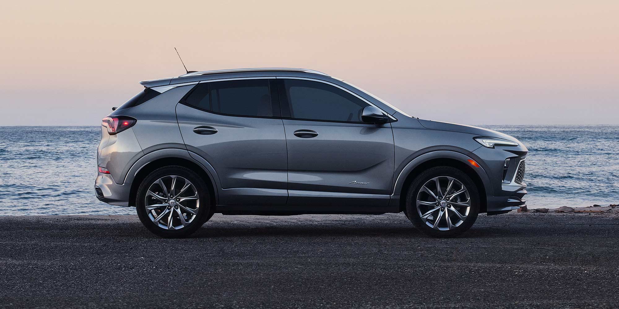 A Silver Buick Encore GX SUV Parked Sideways on a Road with the Calm Ocean at Sunset