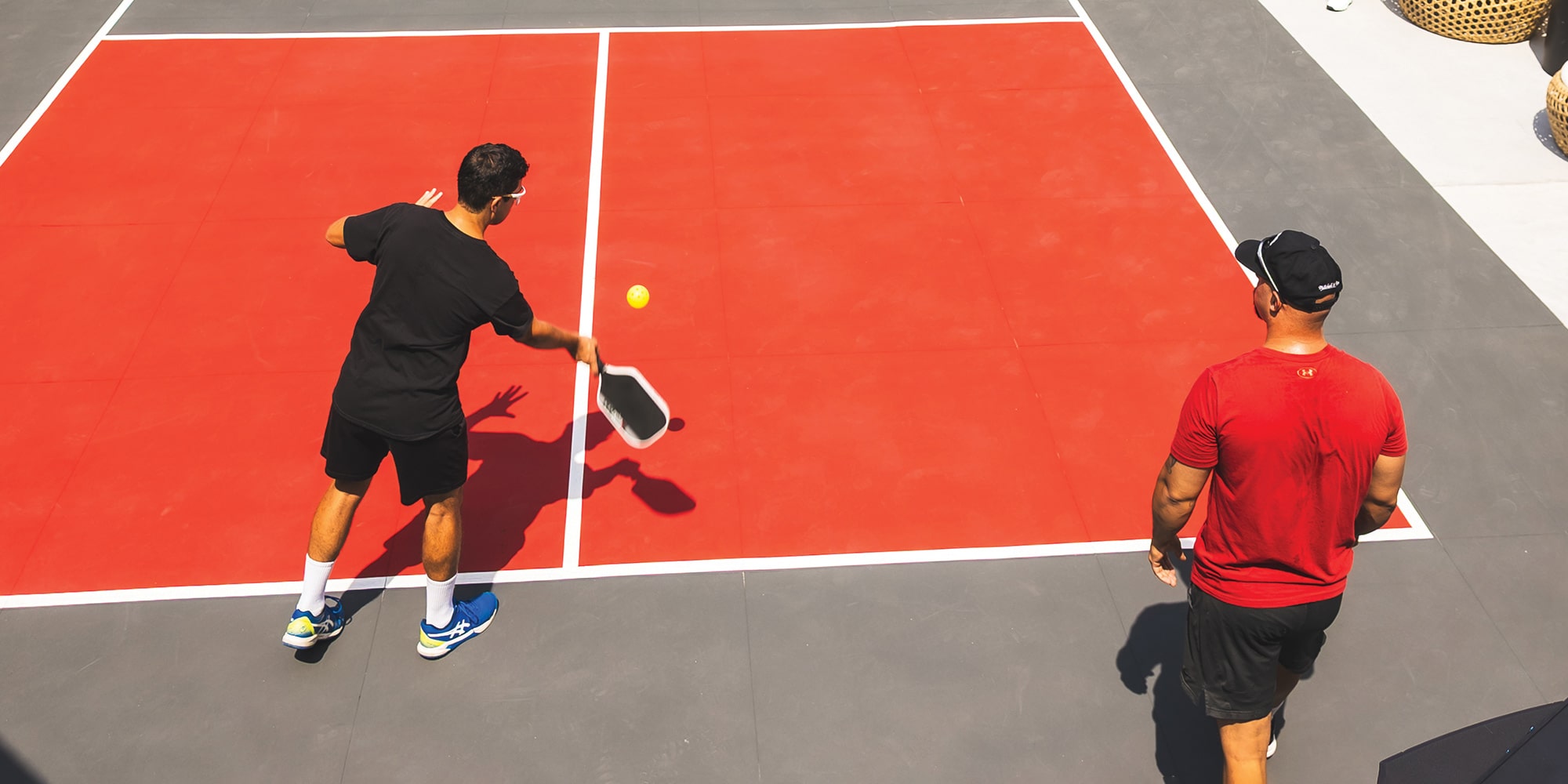 An Aerial View of an Outdoor Pickleball Court with Players and a Blue Buick Vehicle in the Background