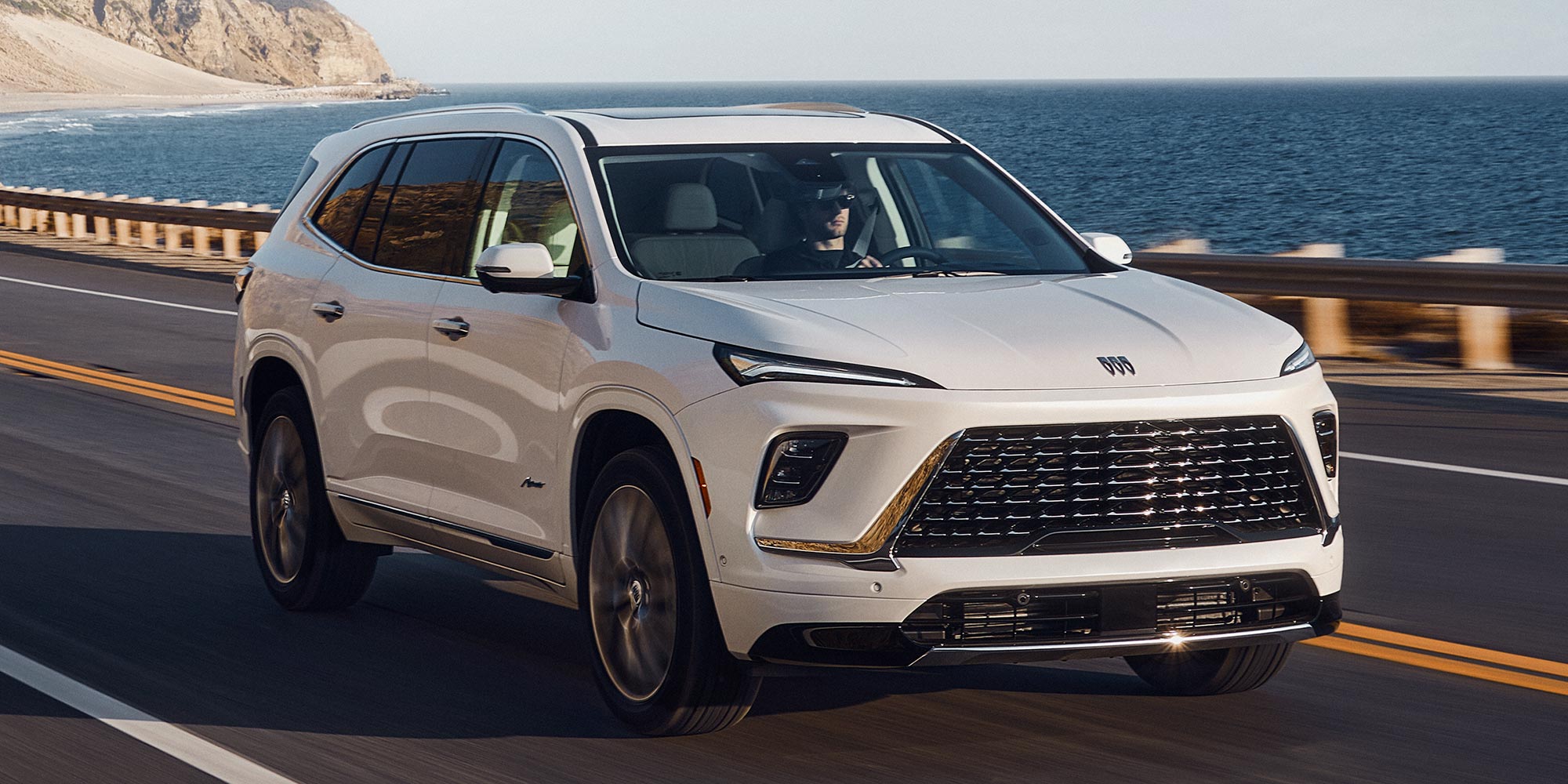 A White Buick SUV Driving on a Scenic Coastal Road with the Ocean and Cliffs