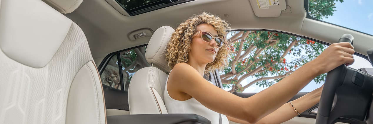 A Stylish Woman with Curly Hair Drives a Buick SUV with the Sunroof Open on a Sunny Day
