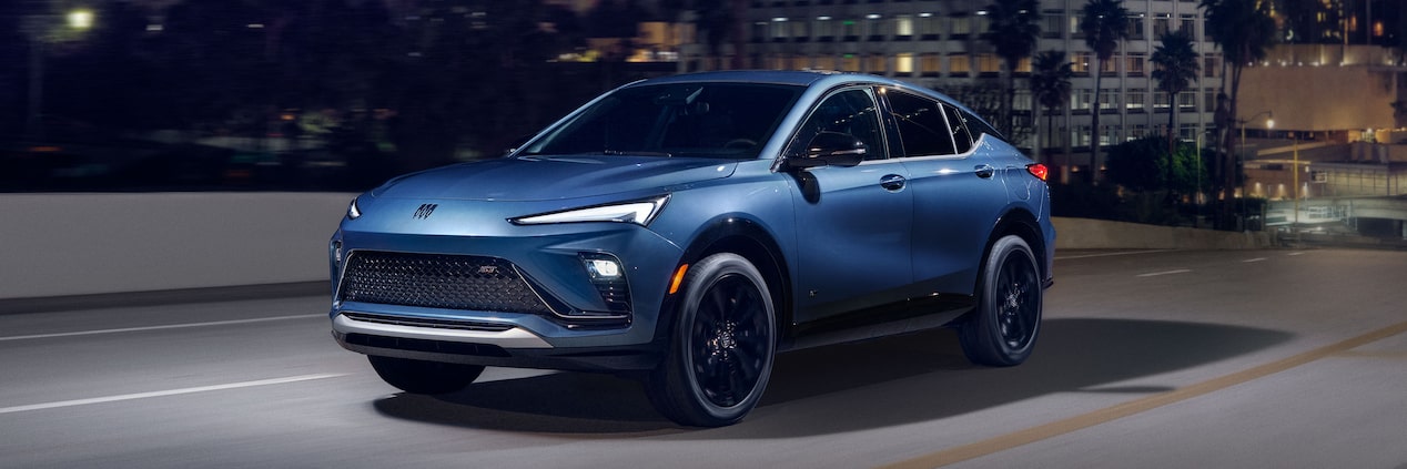 A Blue Buick Envista Compact SUV Driving on a City Street at Night with Its Headlights On