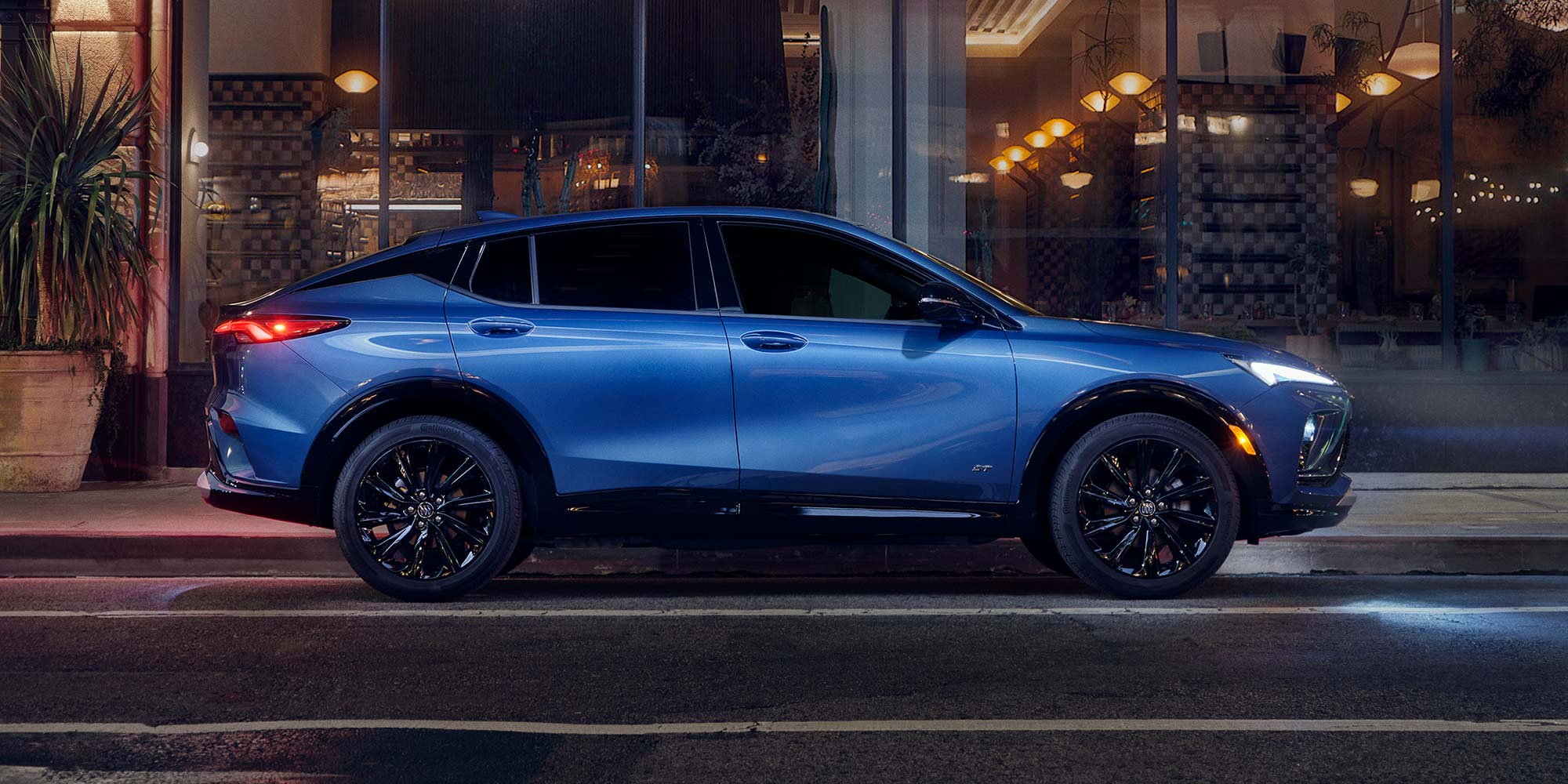 A Blue Buick SUV Is Parked on a City Street at Night, Next to Illuminated Storefronts