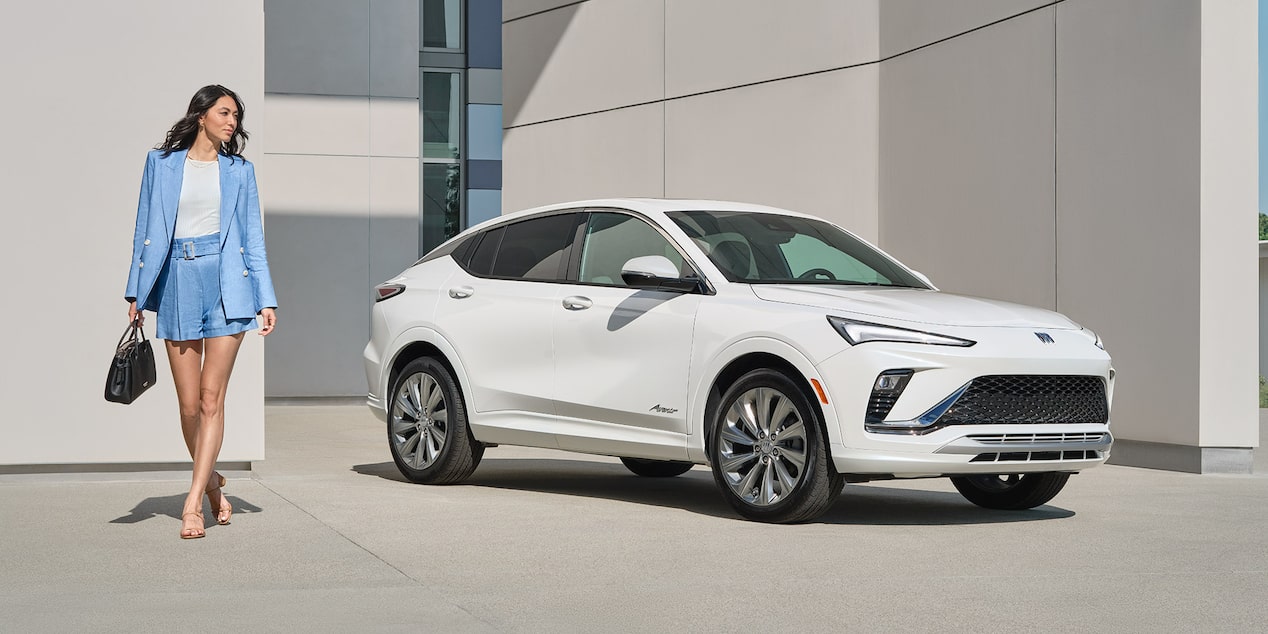 A Woman Walking Beside a White Buick Crossover SUV Parked in Front of a Modern Building
