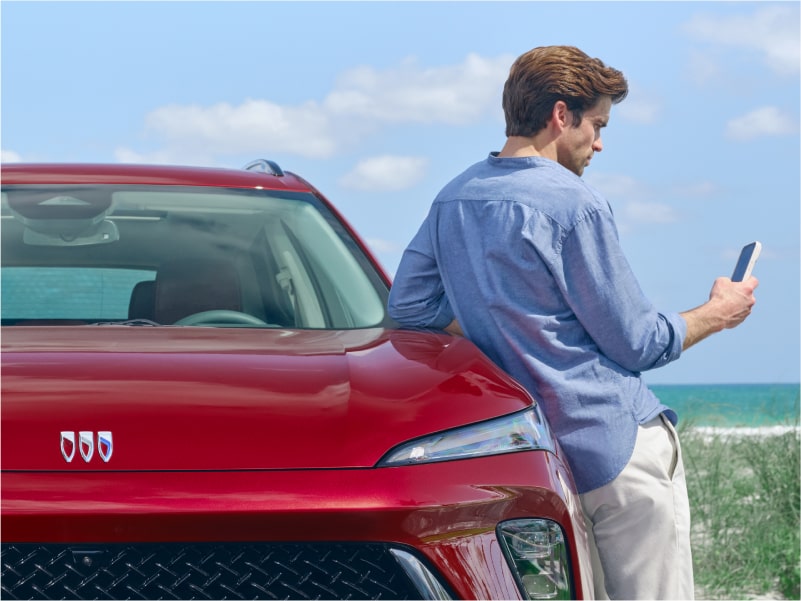 A Man Leaning on the Hood of His Buick Vehicle Using His Smartphone
