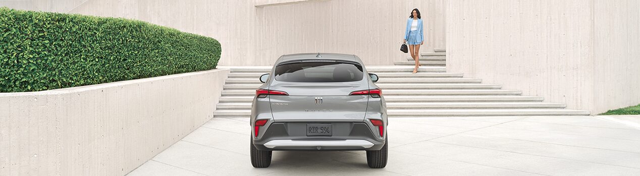 Grey Buick SUV parked in front of stairs with a woman in a blue two piece outfit walking down the stairs