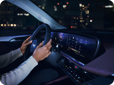 A driver's hands are on the steering wheel of a Buick vehicle at night, with a large illuminated digital screen displaying multiple app icons.