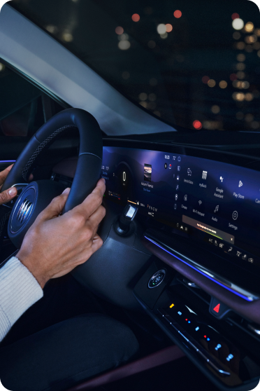 Hands grip the steering wheel of a Buick at night with the digital dashboard illuminated.