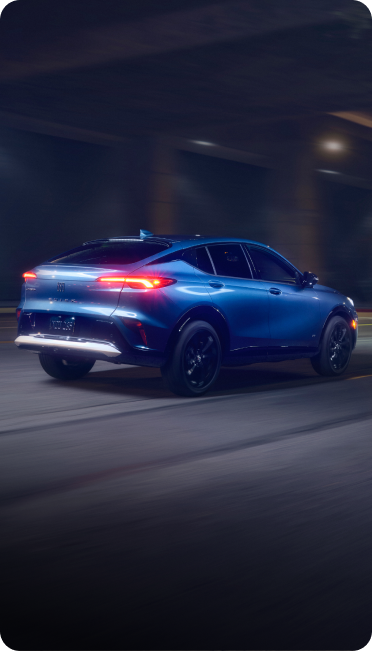 A blue Buick SUV drives down a city street at night under an urban overpass.