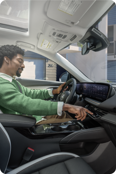 A person wearing a green sweater sits in the driver's seat of a Buick, reaching toward the dashboard controls.