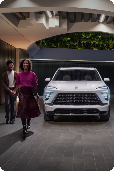 Two people walk toward a modern white Buick SUV parked inside a contemporary garage.