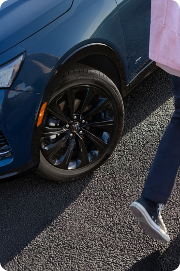 Two people walk past the front wheel and blue body of a Buick vehicle.