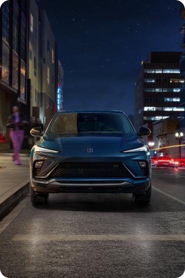 A blue Buick is parked on a city street at night near two people standing on the sidewalk.