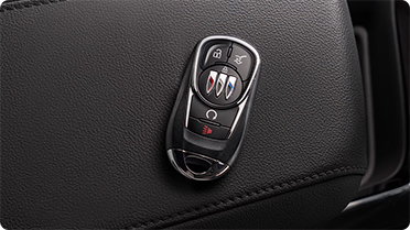 A black Buick key fob with chrome accents and various buttons rests on a textured black leather surface.