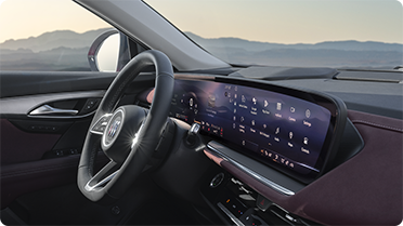 The interior of a Buick vehicle features a wide panoramic digital display and a clear view of mountains and sky through the windshield.