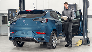 A service technician standing by a blue Buick Encore GX in a service bay while reviewing a tablet.