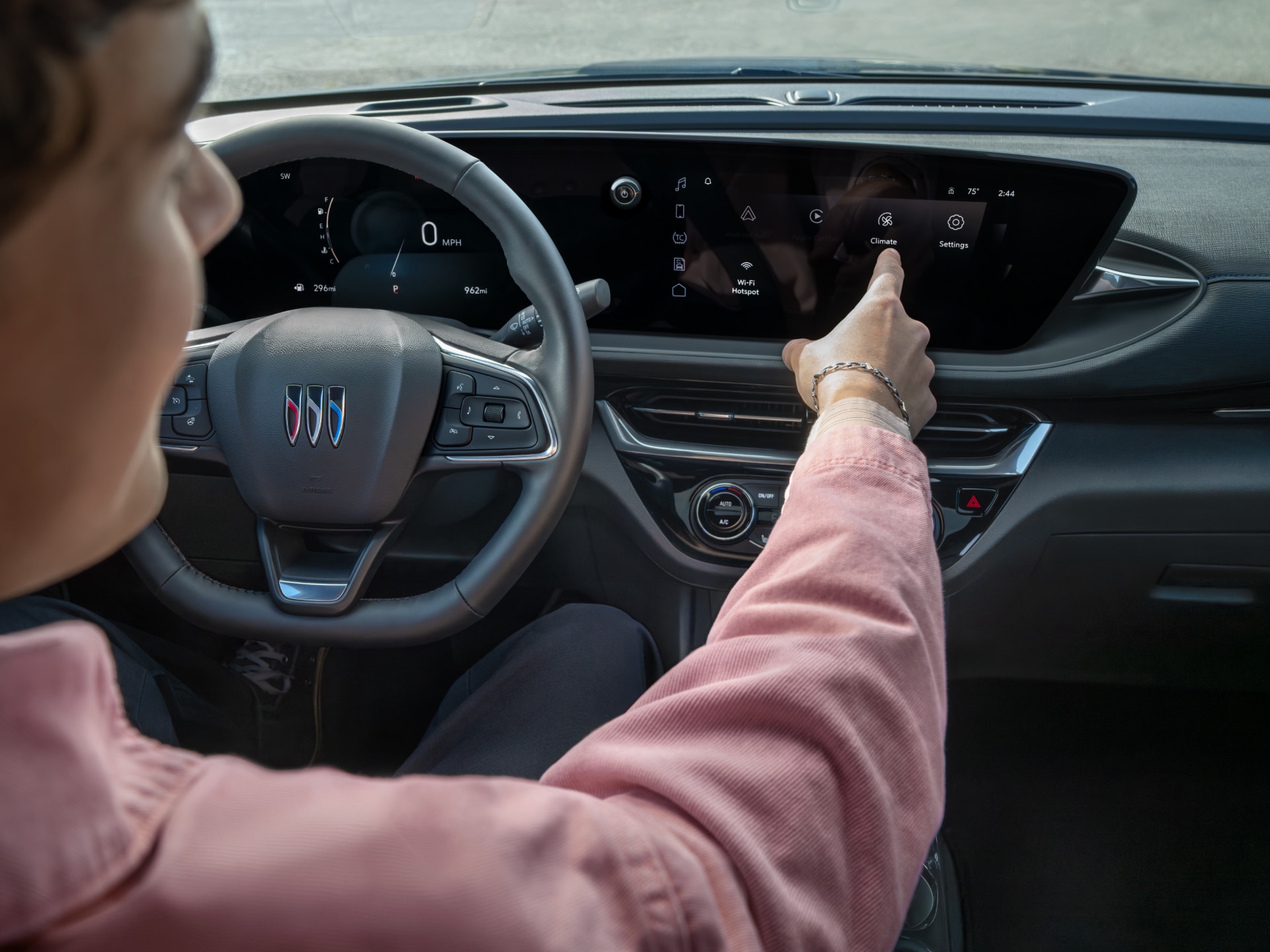 A Person’s Hand Reaching to Touch the Climate Icon on a Buick Vehicle’s Infotainment Screen with the Buick Logo on the Steering Wheel
