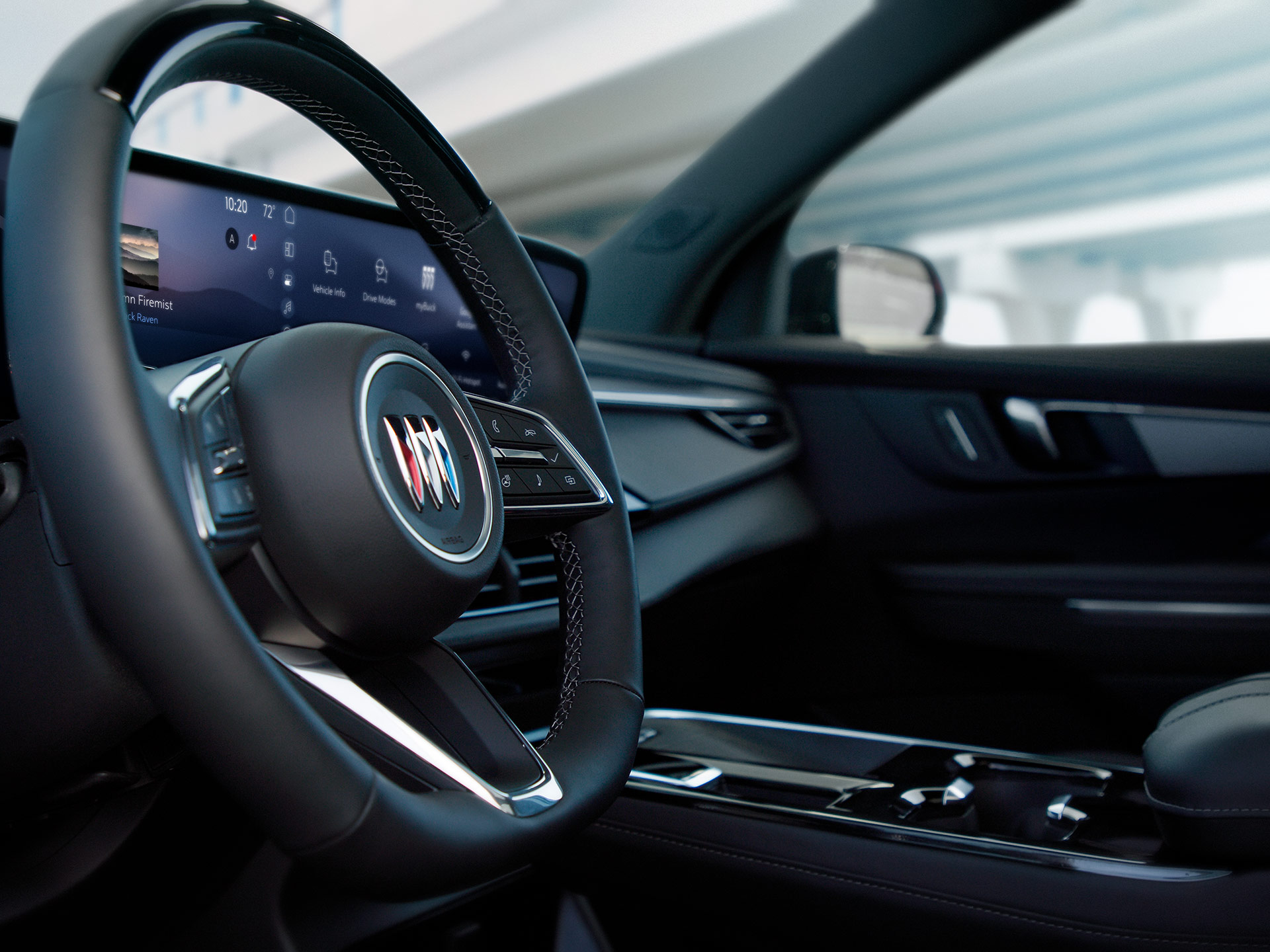 The Modern Interior Dashboard of a Buick Vehicle with a Wide Curved Digital Display and the Buick Logo on the Steering Wheel