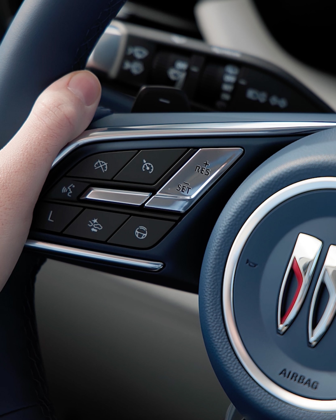 A Hand on the Dark Blue Buick Steering Wheel, Featuring the Buick Trishield Logo and Control Buttons