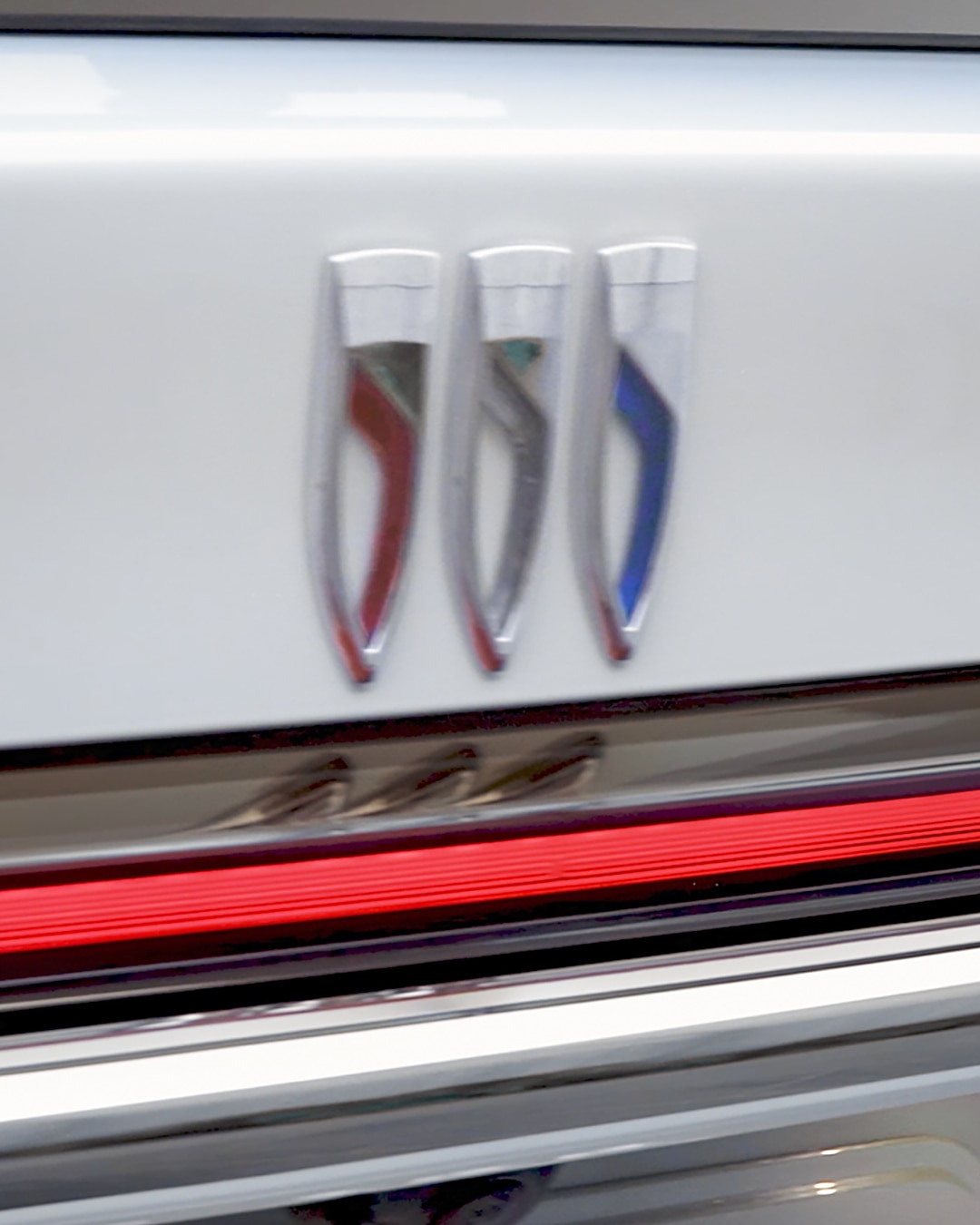 Close-Up of the Rear of a White Buick Vehicle with Illuminated Red Taillights and Three Vertical Buick Trishield Logos