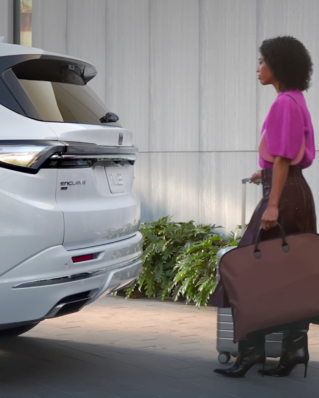 A White Buick Enclave SUV with a Woman Walking Away Carrying Luggage and a Garment Bag