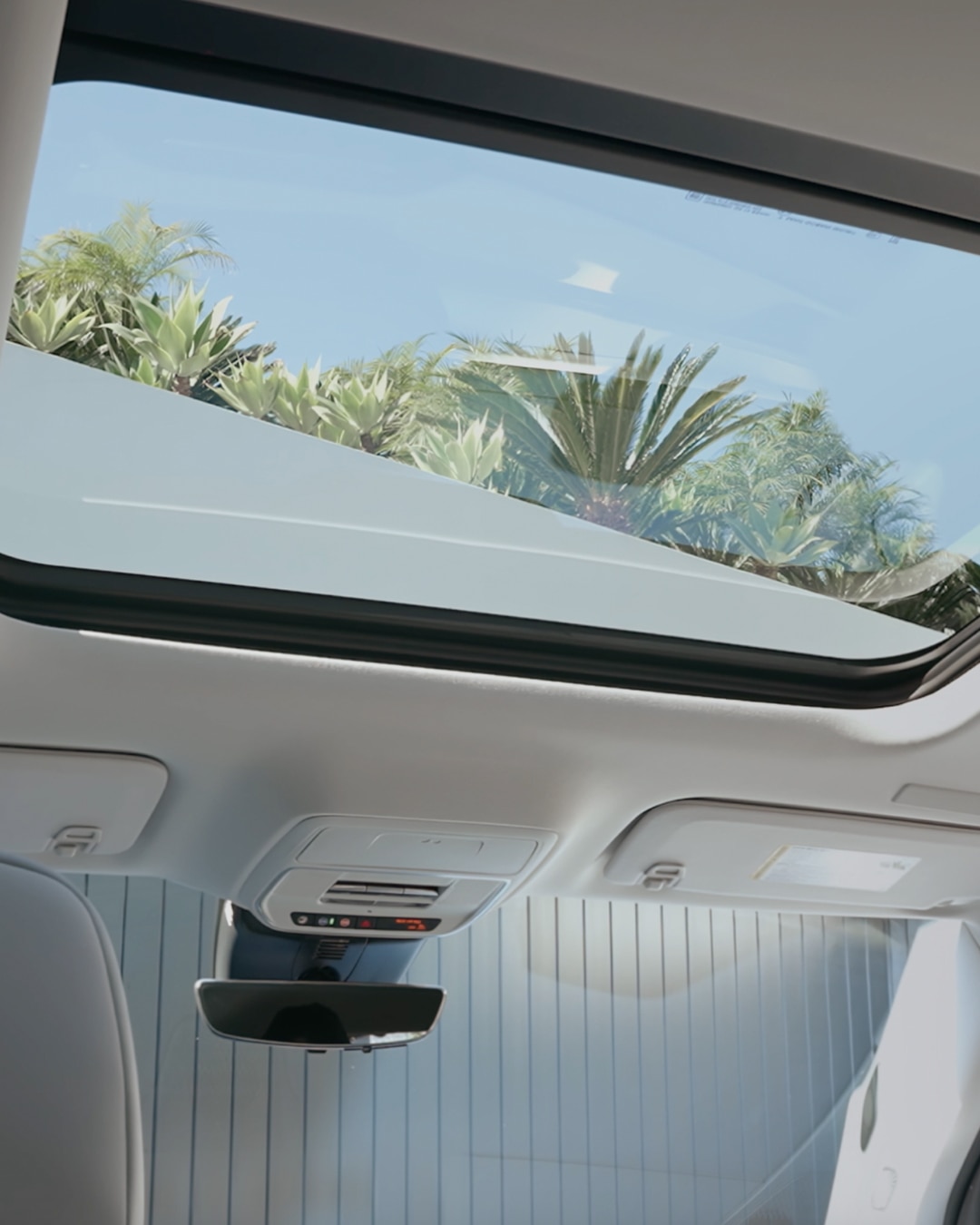 The Interior of a Buick SUV with a Panoramic Sunroof Revealing a Clear Blue Sky and Lush Greenery Outside