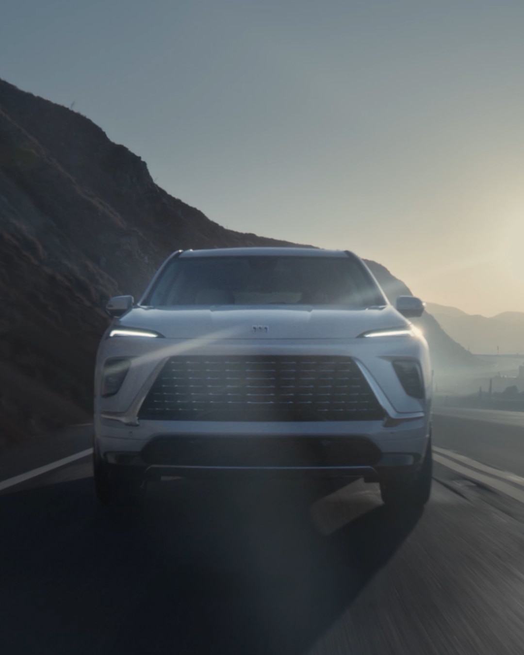 Frontal View of a White Buick Enclave Driving on a Coastal Road at Sunset