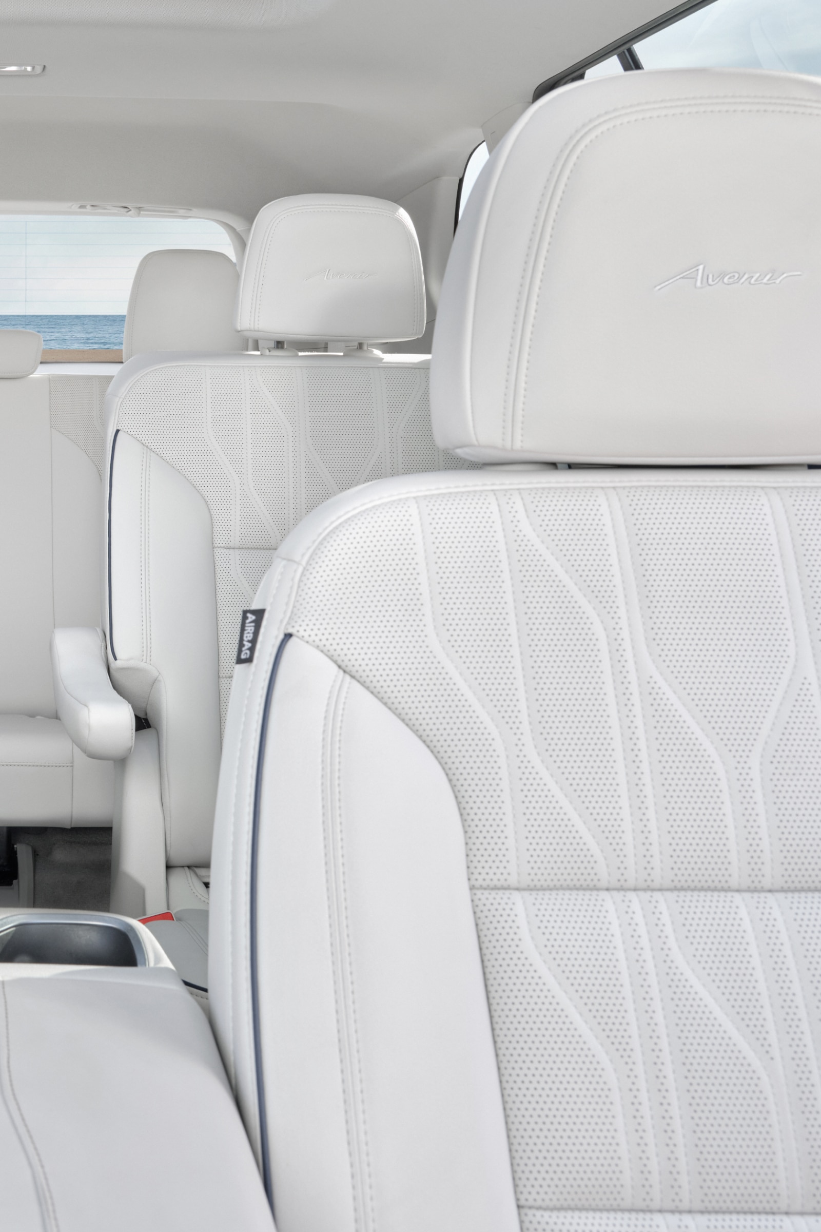 Interior View of a Buick SUV Showing Three Rows of White Seats Facing Towards the Beach and Ocean Through the Rear Window