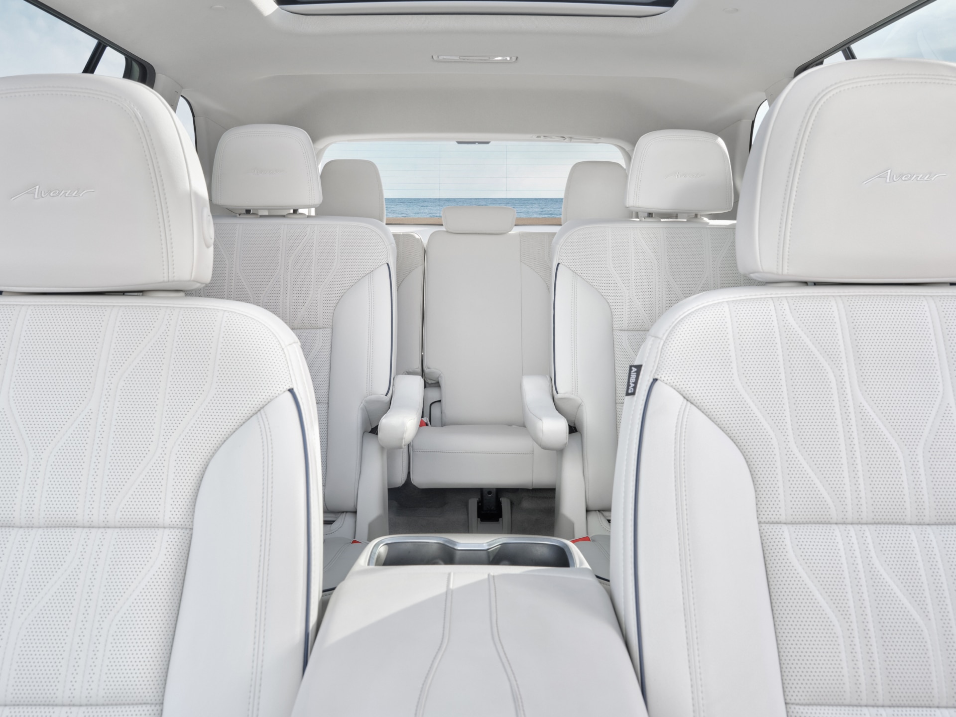 Interior View of a Buick SUV Showing Three Rows of White Seats Facing Towards the Beach and Ocean Through the Rear Window
