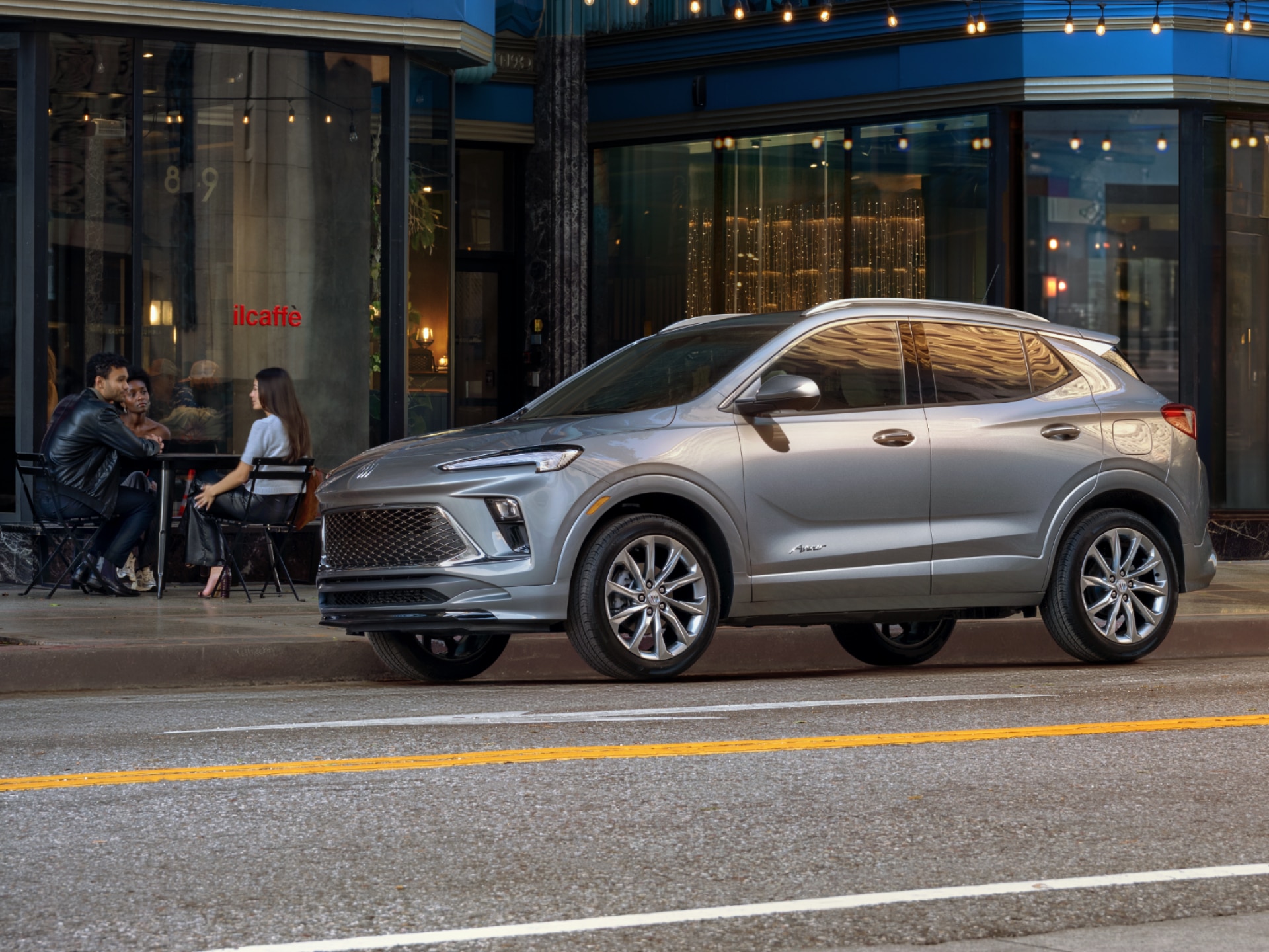 A Gray Buick Encore GX Parked on a City Street Outside a Cafe with People