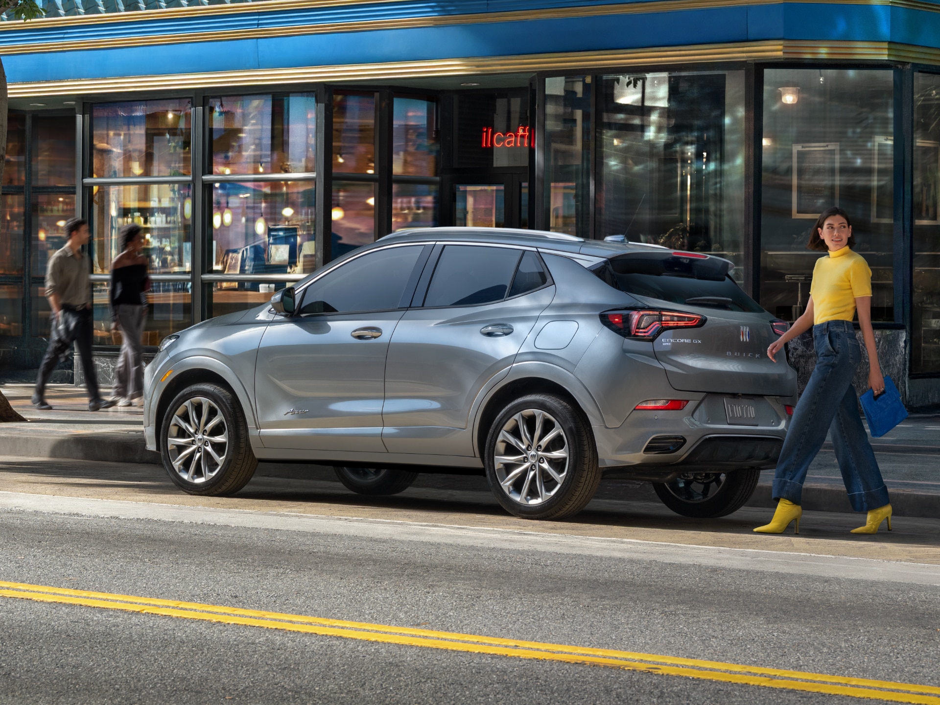 A Woman in a Yellow Top Walking Past a Gray Buick Encore GX Parked Outside a Cafe