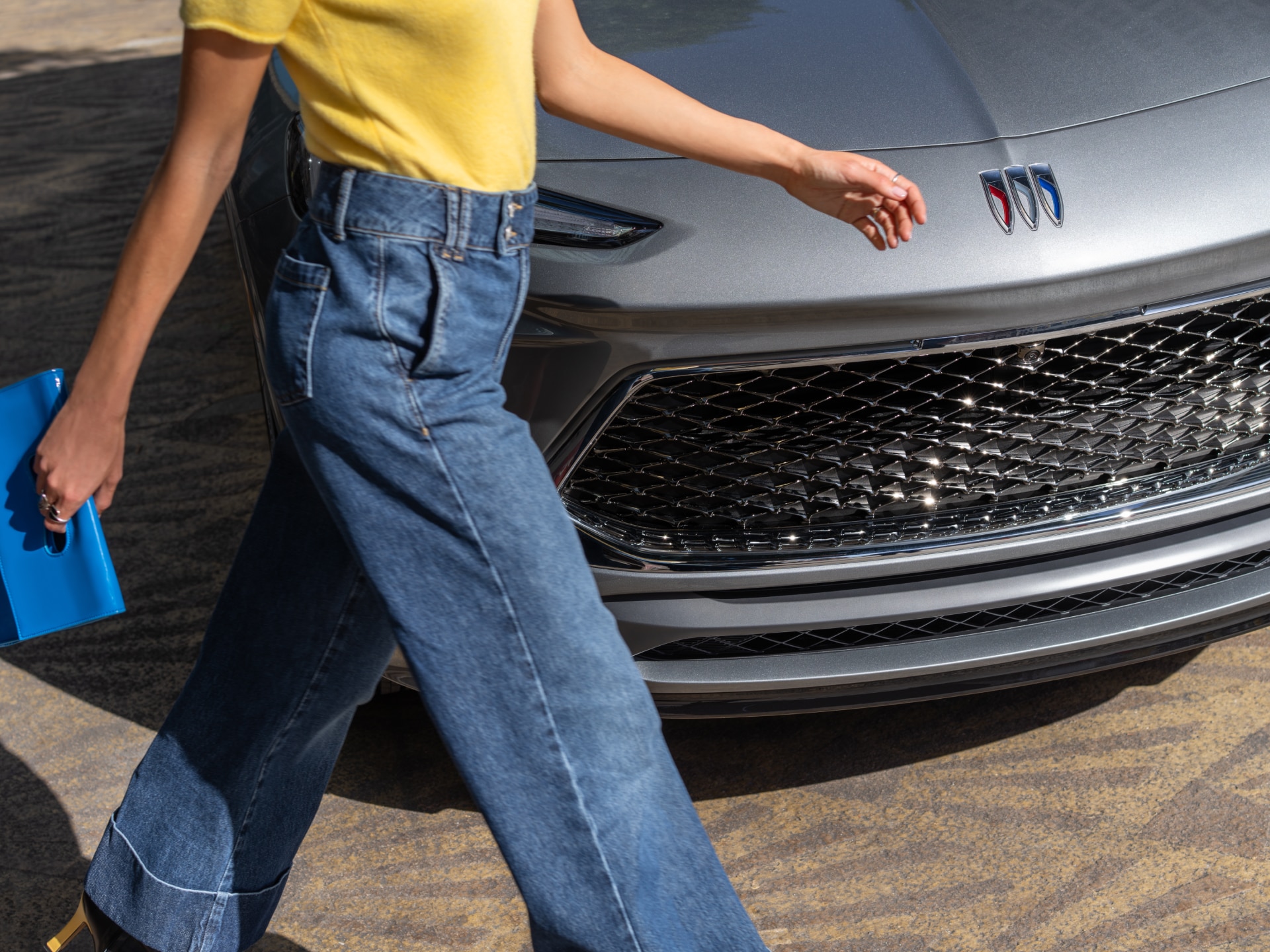 A Woman's Legs in Blue Jeans Walking Past the Front of a Gray Buick Encore GX