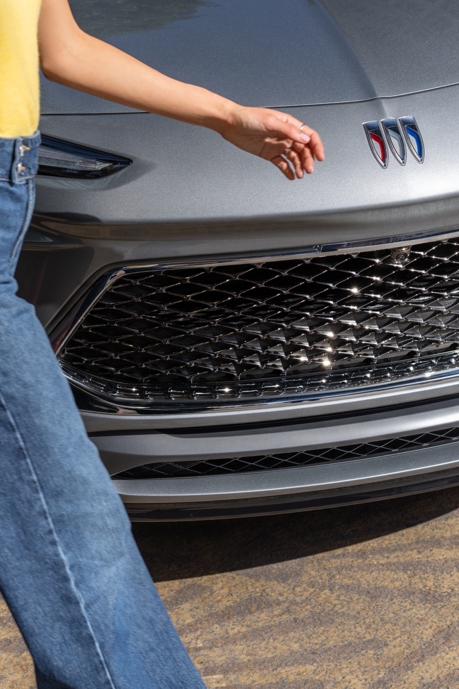 A Woman's Legs in Blue Jeans Walking Past the Front of a Gray Buick Encore GX