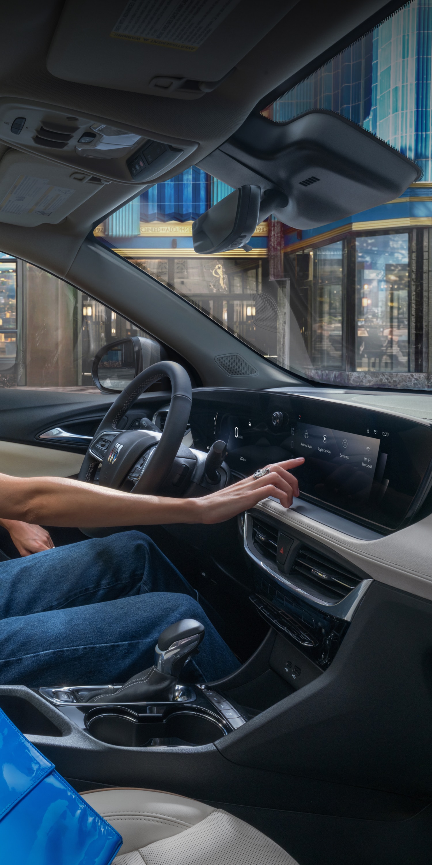 A Woman in a Yellow Shirt Seated in a Buick Vehicle, Smiling While Reaching for the Infotainment Screen