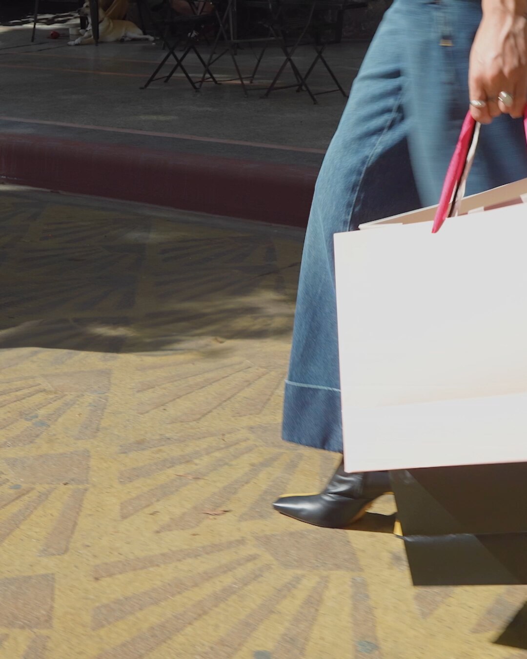 A Person's Legs and Feet Walking with Several Shopping Bags on a Patterned Yellow Sidewalk