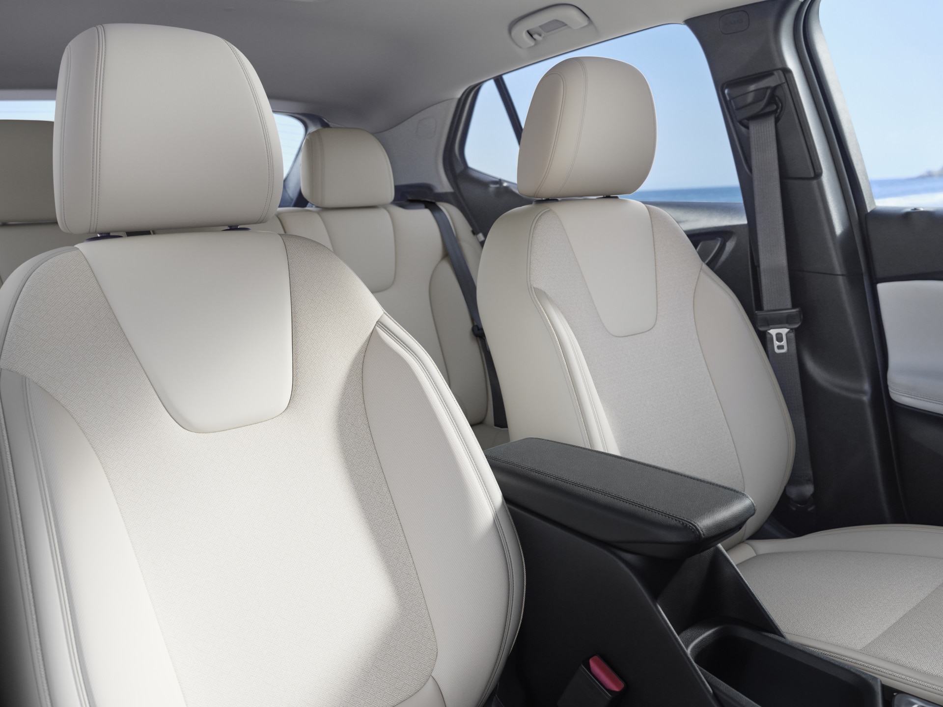The Interior of a Buick Vehicle with Light-Colored Seats and an Armrest with the Ocean in the Background