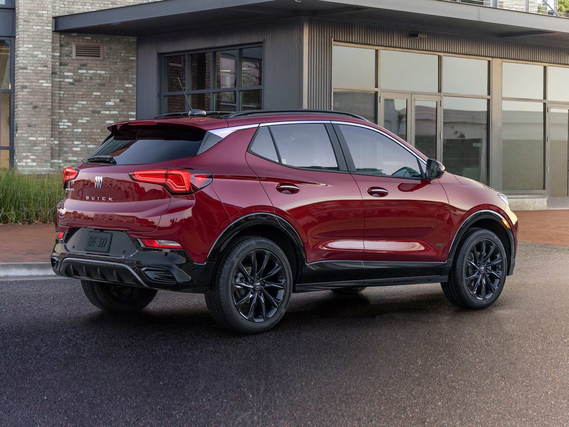 Rear View of a Dark Red Buick Encore GX Parked on a Wet Street in Front of a Modern Building