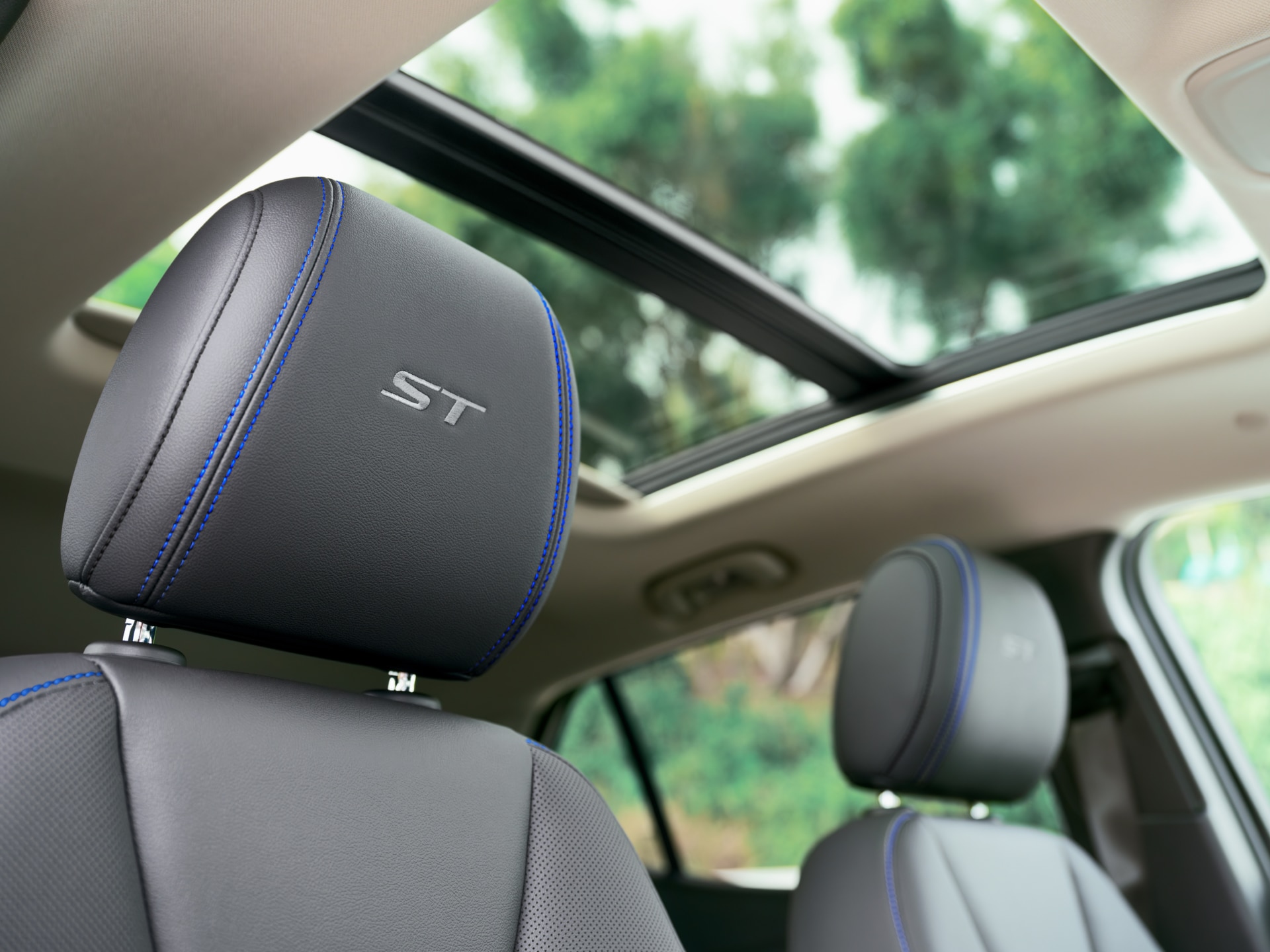 Close-Up of a Black Leather Car Headrest with a Silver 'ST' Logo and Blue Stitching, Featuring a Panoramic Sunroof Above