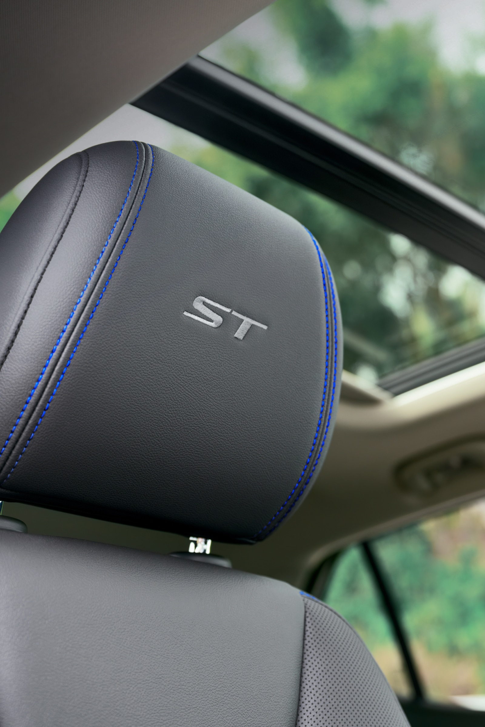 Close-Up of a Black Leather Car Headrest with a Silver 'ST' Logo and Blue Stitching, Featuring a Panoramic Sunroof Above