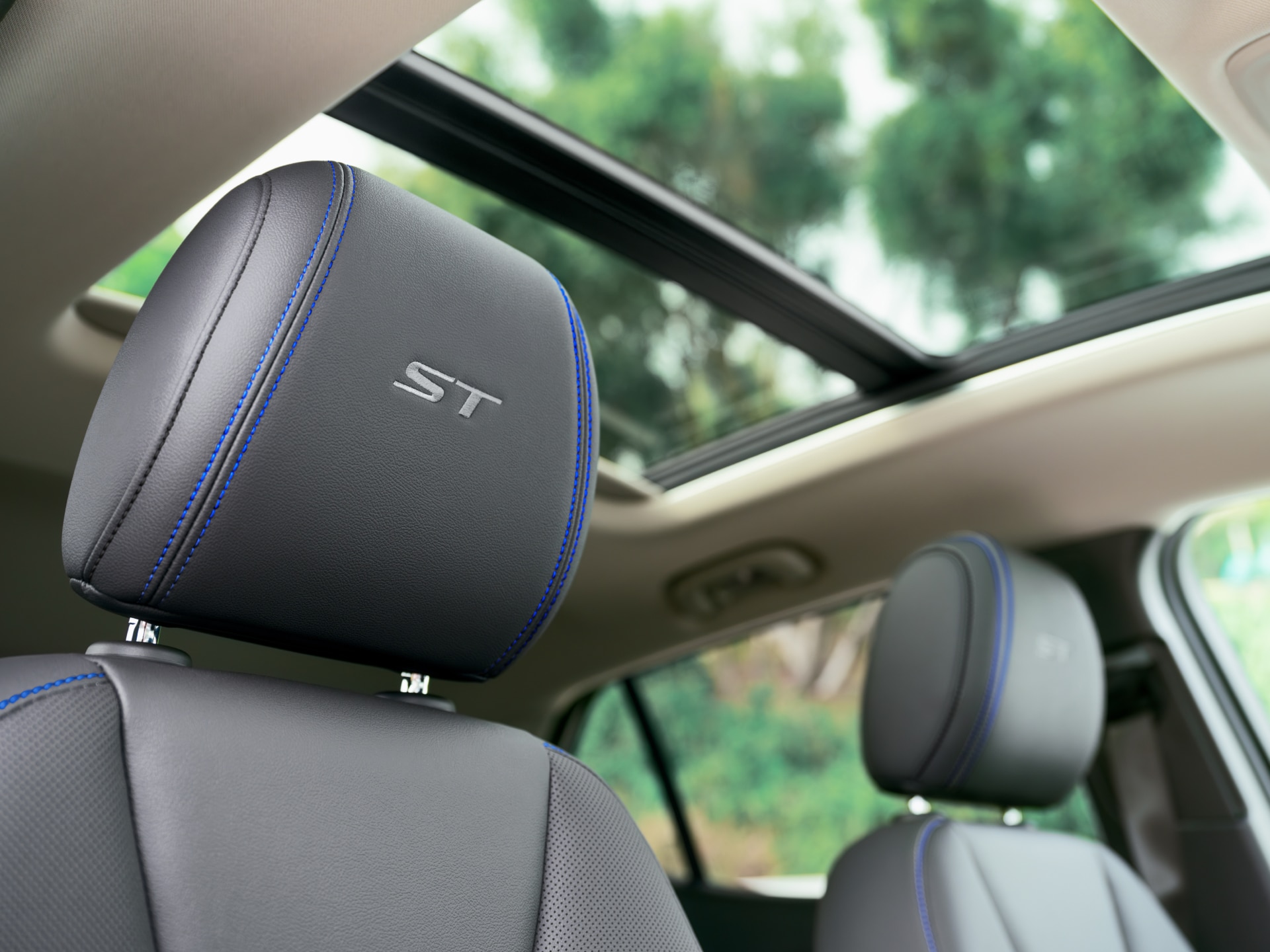 Close-Up of a Black Leather Car Headrest with a Silver 'ST' Logo and Blue Stitching, Featuring a Panoramic Sunroof Above