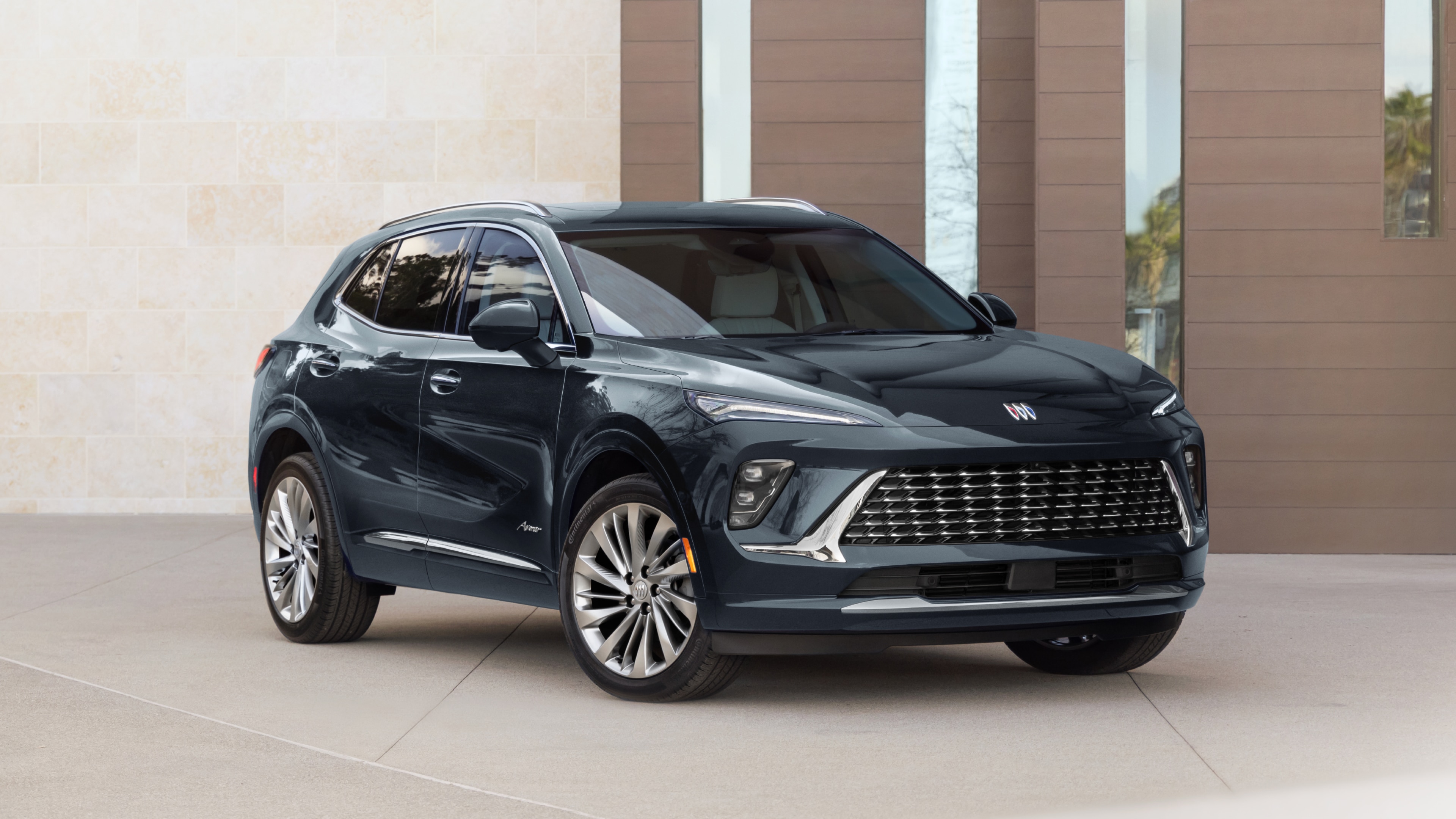 A Dark Blue Buick SUV Angled Towards the Left with a Modern Building in the Background