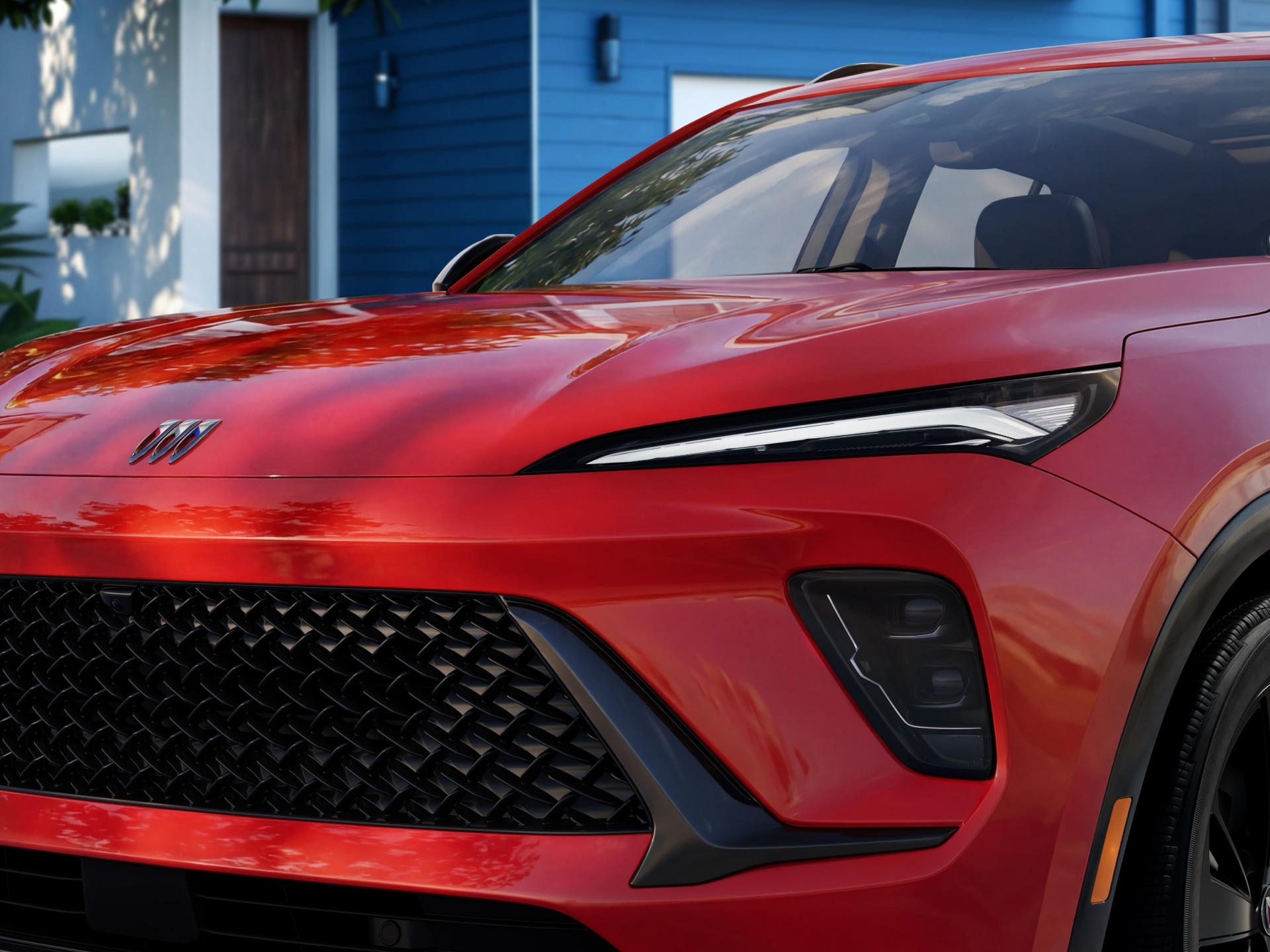 Close-Up of the Front Grille and Headlights of a Red 2027 Buick Envision Parked in Front of a Blue House