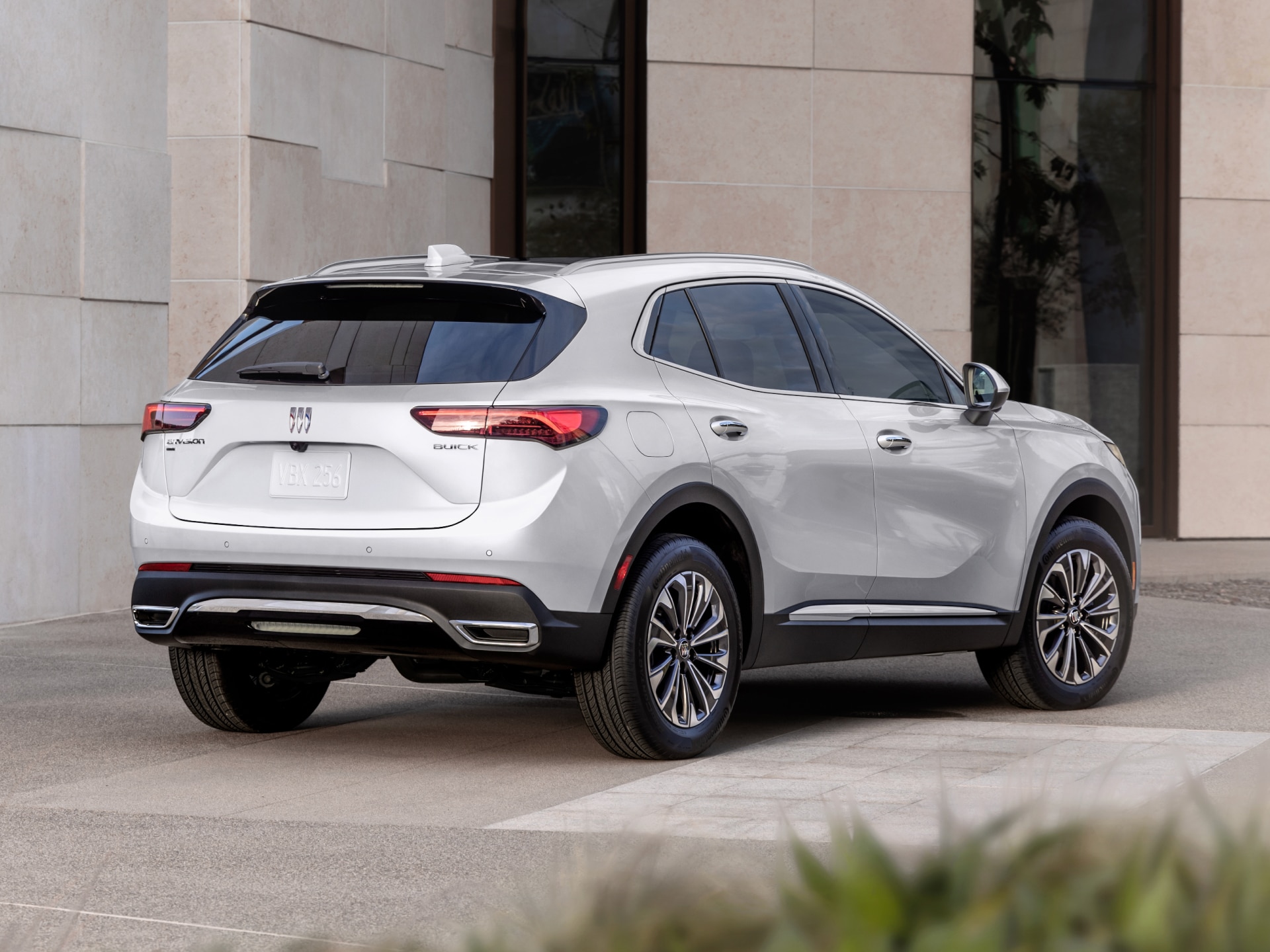The Rear Three Quarter View of a White 2027 Buick Envision Parked in a Driveway Next to a Modern Building
