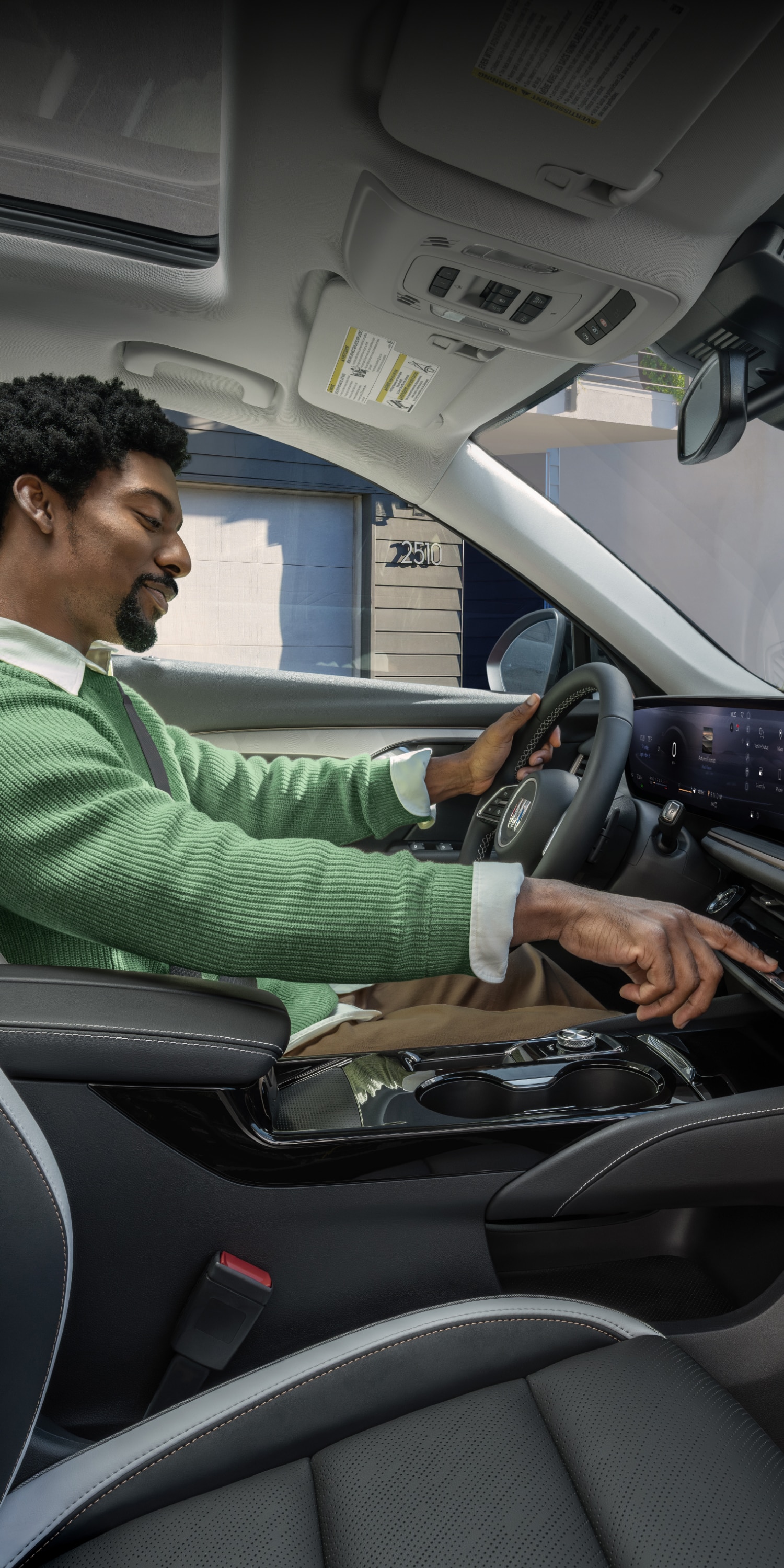 A Man in a Green Sweater Operating the Controls in the Luxurious Interior of a Buick Vehicle with a Panoramic Sunroof and Digital Displays