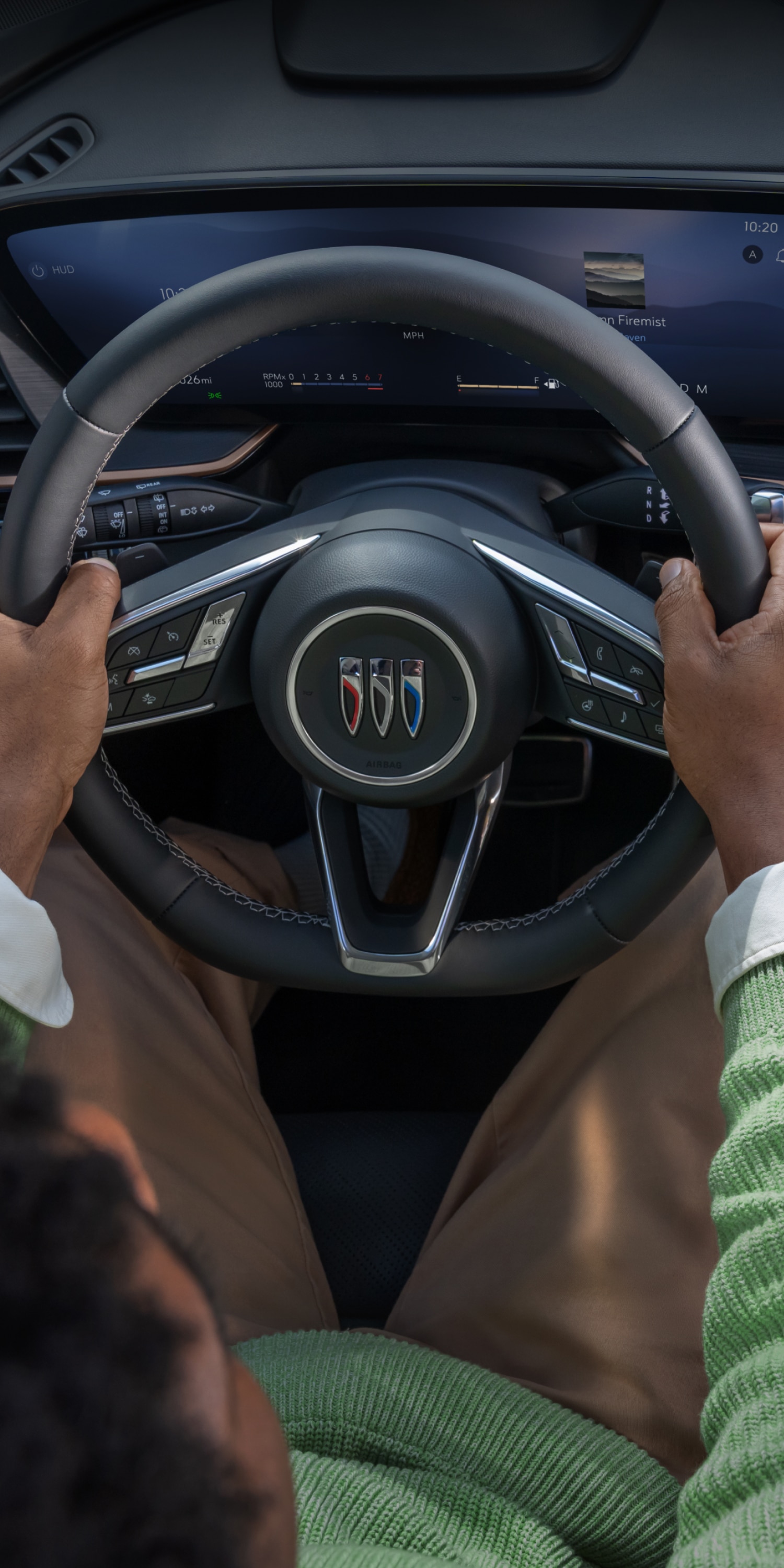 A Driver's Hands on the Steering Wheel of a Buick with a Large Curved Digital Display and Bronze Trim