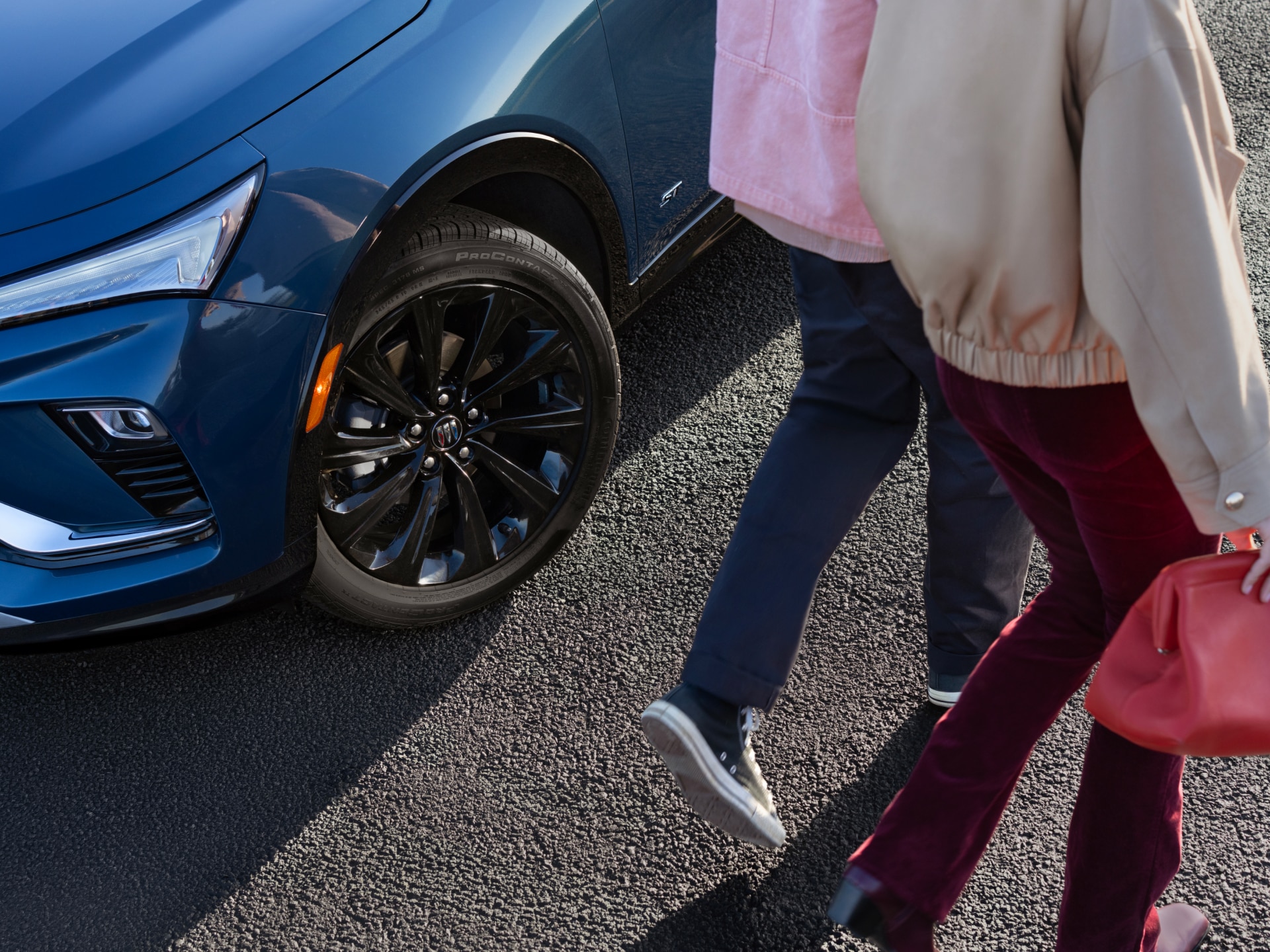Two People Walking Past the Front Passenger Side Wheel of a Dark Blue Buick Envista on an Asphalt Street