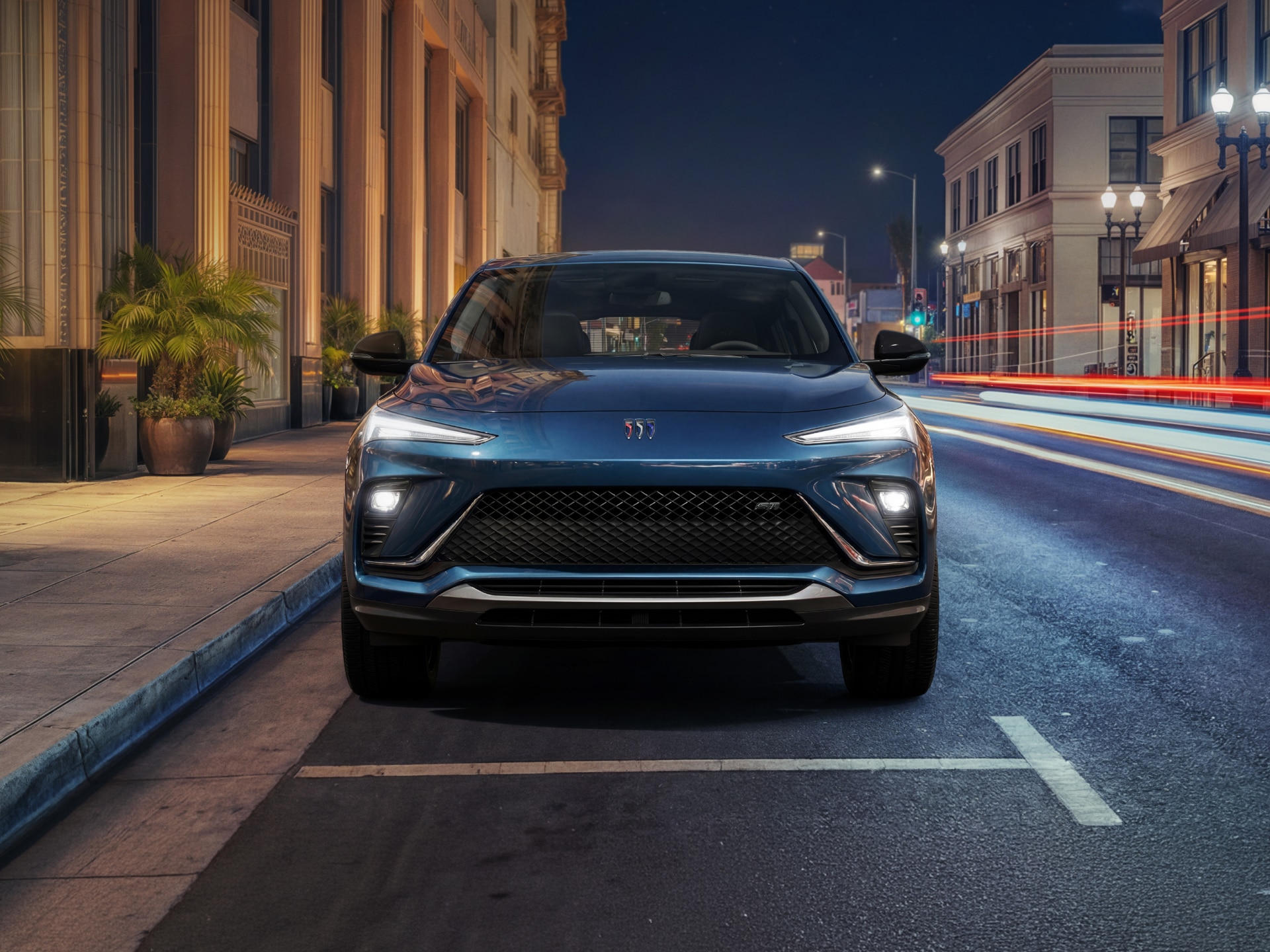 The Front View of a Dark Blue Buick Envista Parked on a City Street At Night with Building Lights and Traffic Streaks