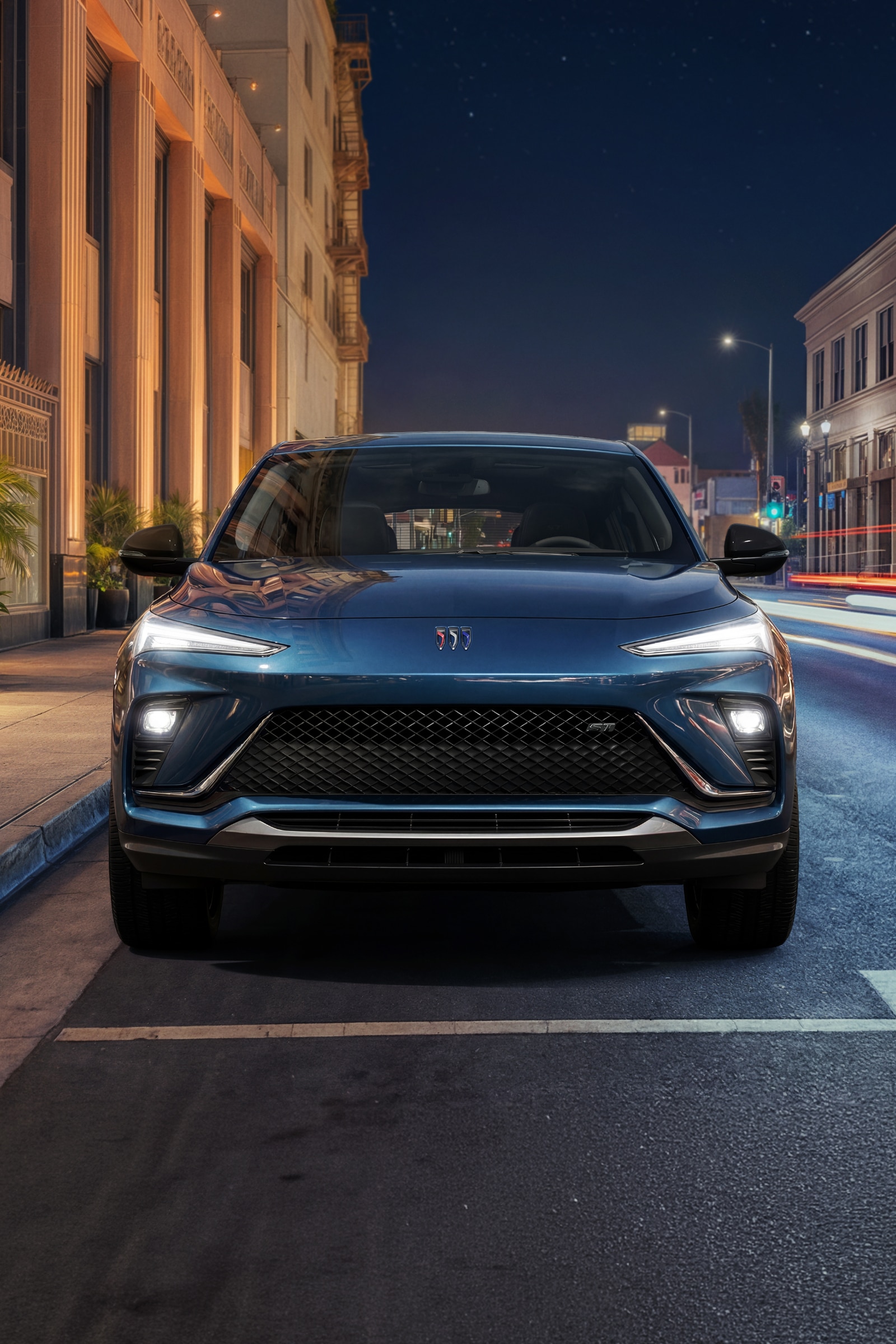 The Front View of a Dark Blue Buick Envista Parked on a City Street At Night with Building Lights and Traffic Streaks