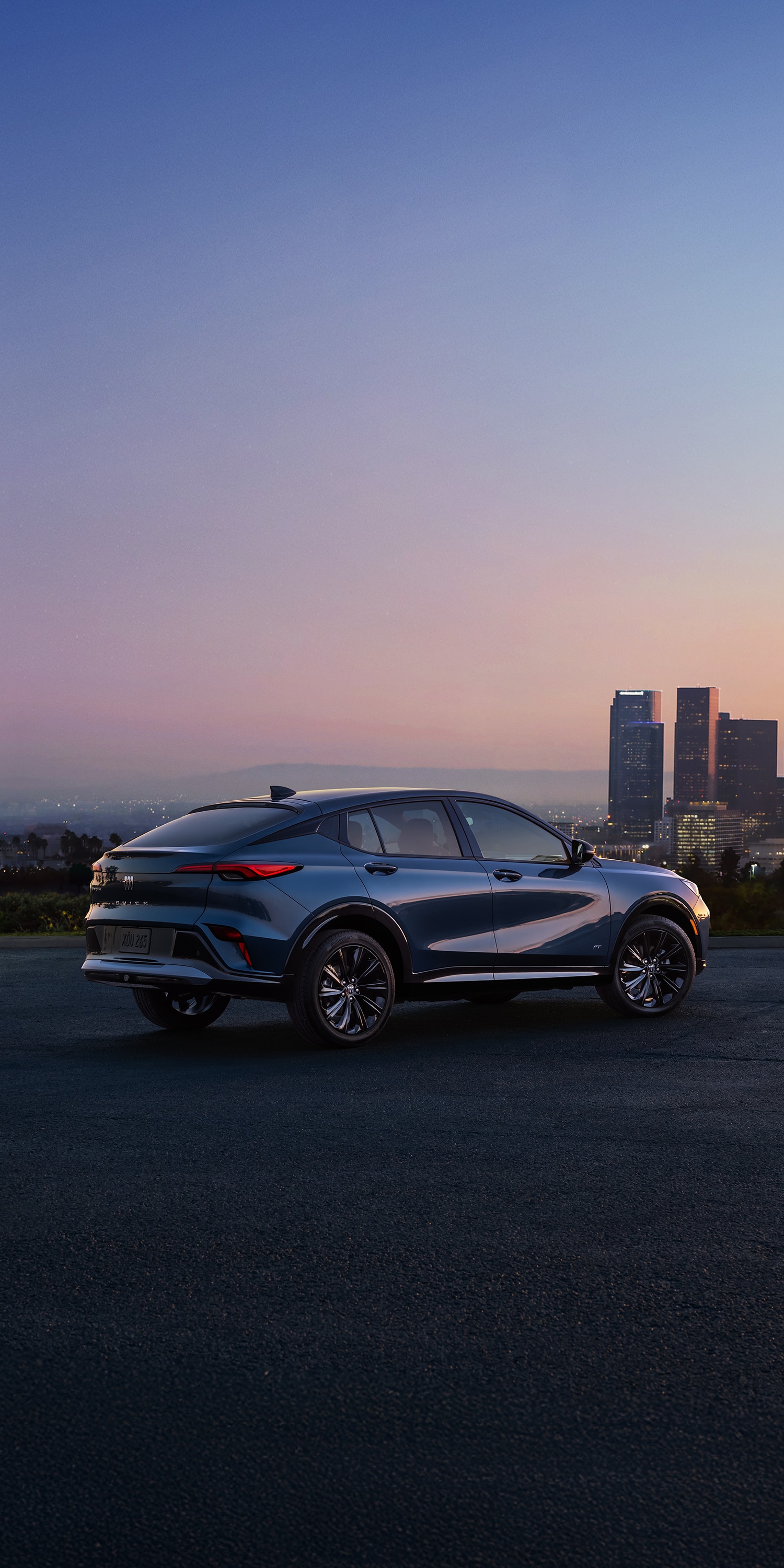 A Blue Buick Envista ST Parked on an Asphalt Surface with a City Skyline and Hazy Horizon in the Background