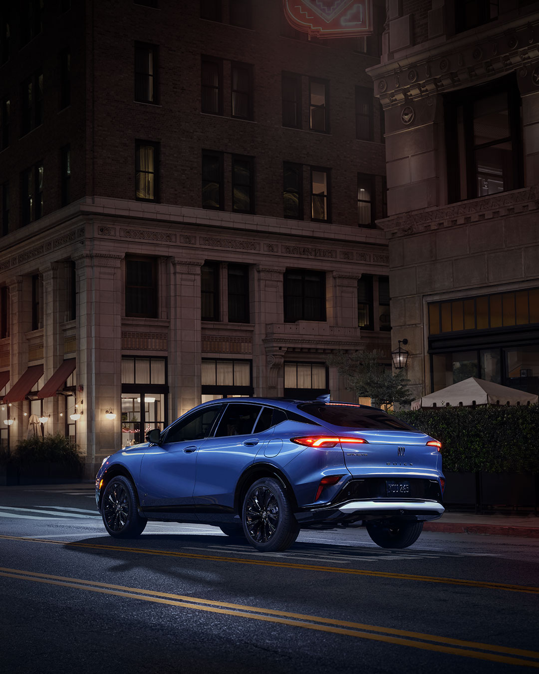A Blue Buick Envista SUV with a Man and Woman Walking by it at Night