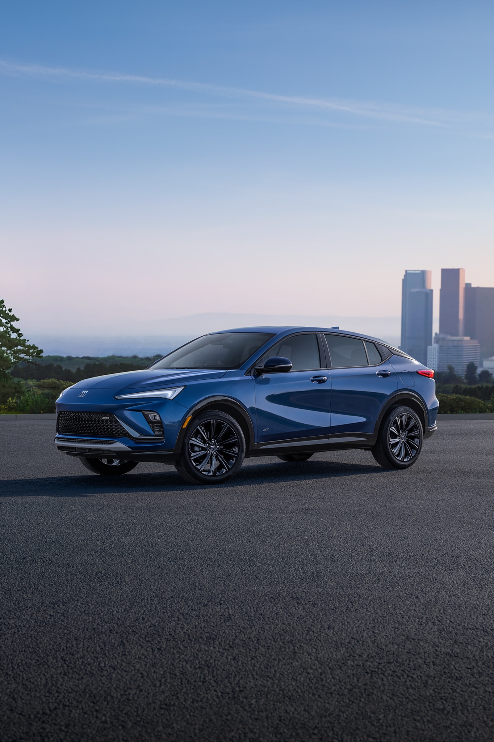 A Blue Buick Envista ST Parked on an Asphalt Surface with a City Skyline and Hazy Horizon in the Background